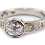 Oval rose cut diamond with gypsy set diamonds in beaten 19 karat white gold.